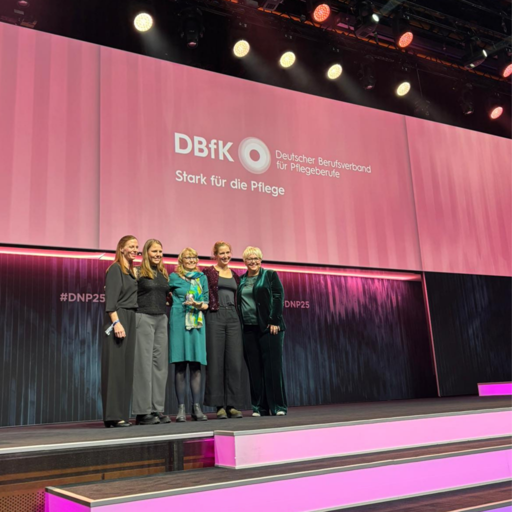 Fünf Frauen stehen auf einer Bühne vor einer großen Leinwand mit dem Logo des Deutschen Berufsverbands für Pflegeberufe und dem Text 'Stark für die Pflege'.